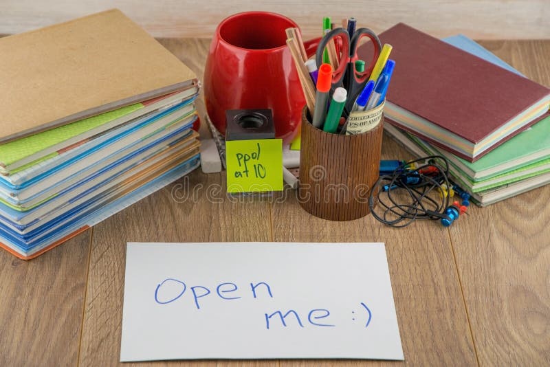 Student desktop, books, accessories, stationery, mug, in the foreground mysterious envelope with the words ` open me. Student desktop, books, accessories, stationery, mug, in the foreground mysterious envelope with the words ` open me