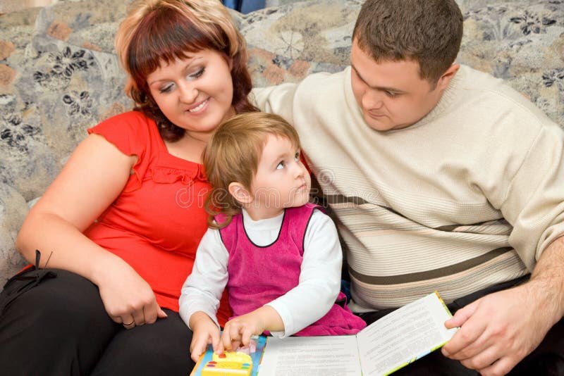 Married couple and little girl read book in cosy room, indoor. Married couple and little girl read book in cosy room, indoor