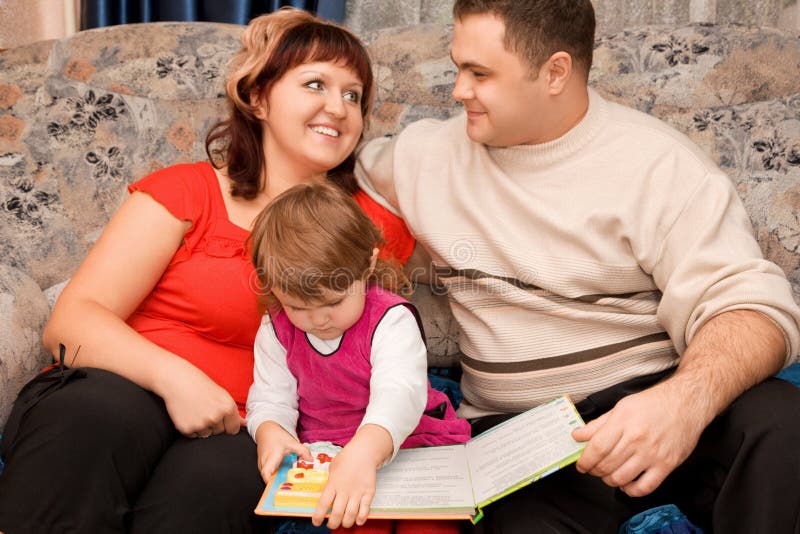 Happy married couple and little girl read book in a cosy room. Happy married couple and little girl read book in a cosy room