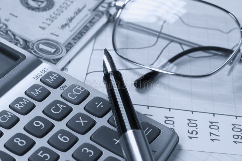 A calculator, reading glasses and pen on top of financial reports. A calculator, reading glasses and pen on top of financial reports.