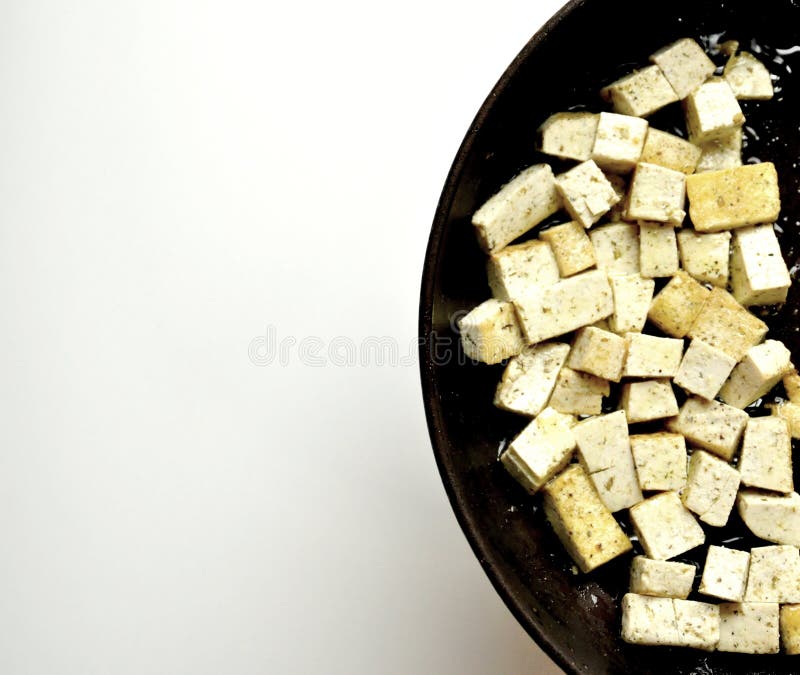 Cooking tofu in a pan on a white background. Tofu pieces beeing cooked in olive oil. vegetarian, vegan diet concept. Cooking tofu in a pan on a white background. Tofu pieces beeing cooked in olive oil. vegetarian, vegan diet concept.