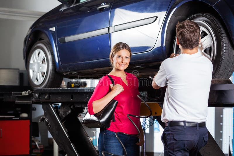 Portrait of smiling female customer standing with mechanic refilling tire at garage. Portrait of smiling female customer standing with mechanic refilling tire at garage