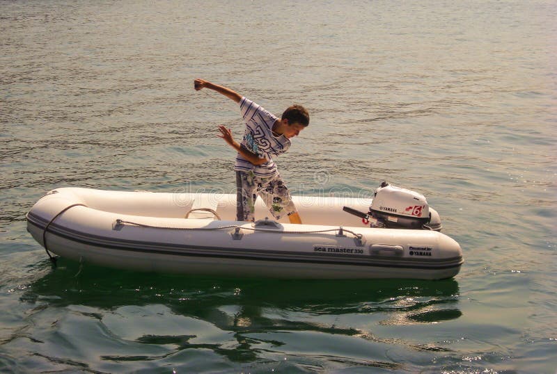 Kusadasi, Turquia - 17 de junho de 2012: um menino está ligando o motor externo do barco inflável imagem de stock royalty free Kusadasi, Turquia - 17 de junho de 2012: um menino está ligando o motor externo do barco inflável imagem de stock royalty free