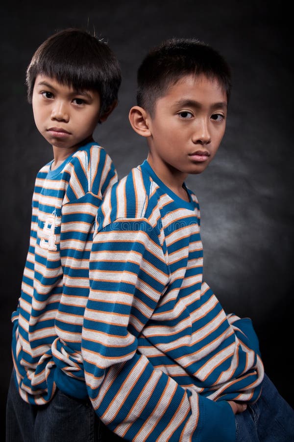 Two young eleven year old asian boys standing with backs together wearing matching shirts. Two young eleven year old asian boys standing with backs together wearing matching shirts