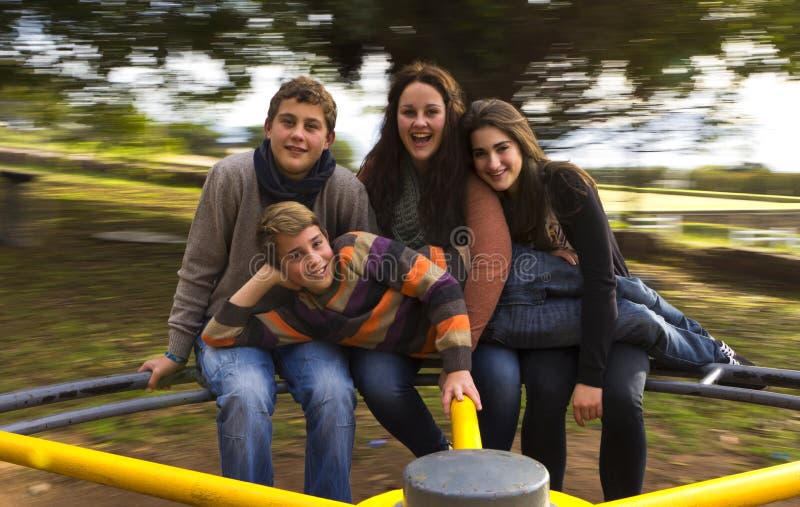 Four cousins on a merry go round outside spinning. Motion visible in image and smiling teens. Four cousins on a merry go round outside spinning. Motion visible in image and smiling teens.