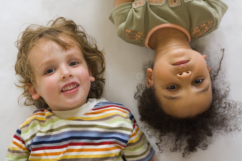 A young blond boy and a beautiful mixed race little girl looking up into the camera. A young blond boy and a beautiful mixed race little girl looking up into the camera