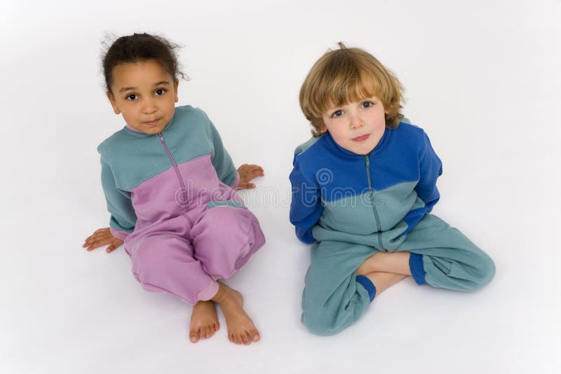 A beautiful mixed race little girl and a blonde boy dressed in sleep suits look up into the camera. A beautiful mixed race little girl and a blonde boy dressed in sleep suits look up into the camera