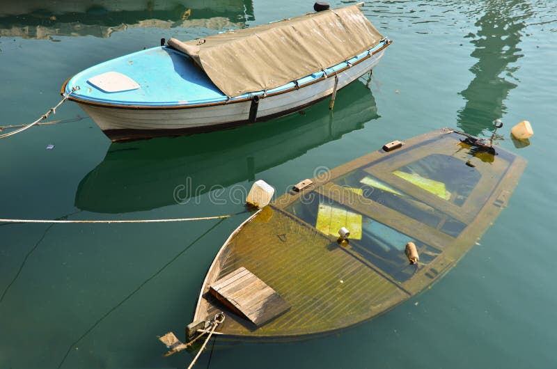 Two boats on berth, plastic blue one, and wooden one is sinking. Two boats on berth, plastic blue one, and wooden one is sinking