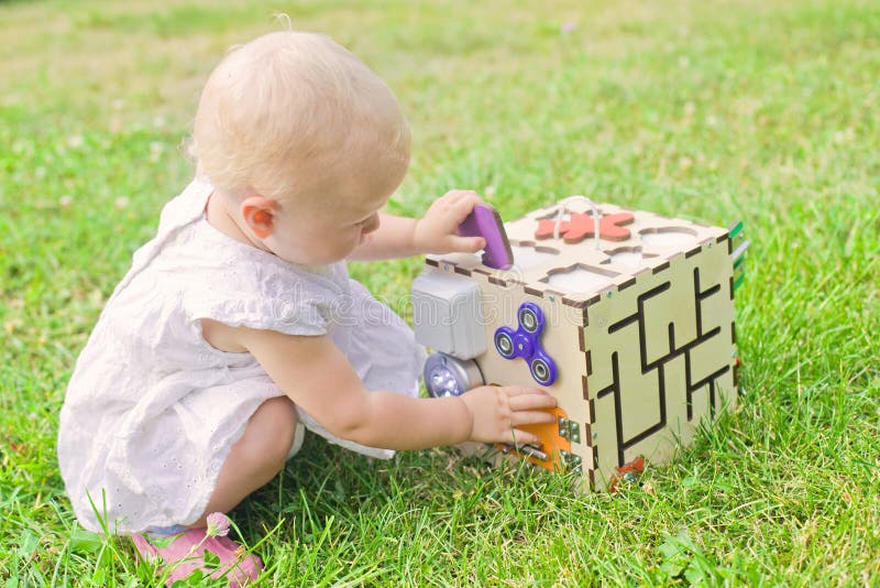 Kute little girl speelt met buitenshuis op groengras. Educatief speelgoed voor peuters meisje opende de deur voor de kubus van stock foto Kute little girl speelt met buitenshuis op groengras. Educatief speelgoed voor peuters meisje opende de deur voor de kubus van stock foto