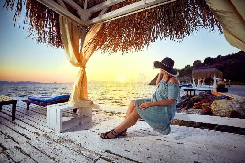 Kvinna i hatt som kopplar av vid havet i en lyxig beachfront hotellsemesterort på solnedgången som in tycker om perfekt strandfer fotografering för bildbyråer Kvinna i hatt som kopplar av vid havet i en lyxig beachfront hotellsemesterort på solnedgången som in tycker om perfekt strandfer fotografering för bildbyråer
