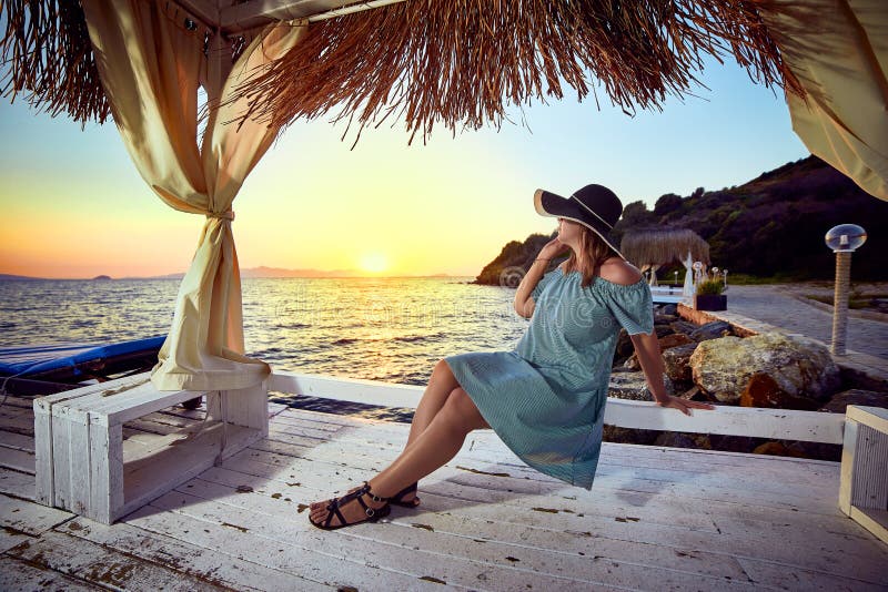 Kvinna i hatt som kopplar av vid havet i en lyxig beachfront hotellsemesterort på solnedgången som in tycker om perfekt strandfer royaltyfri foto Kvinna i hatt som kopplar av vid havet i en lyxig beachfront hotellsemesterort på solnedgången som in tycker om perfekt strandfer royaltyfri foto