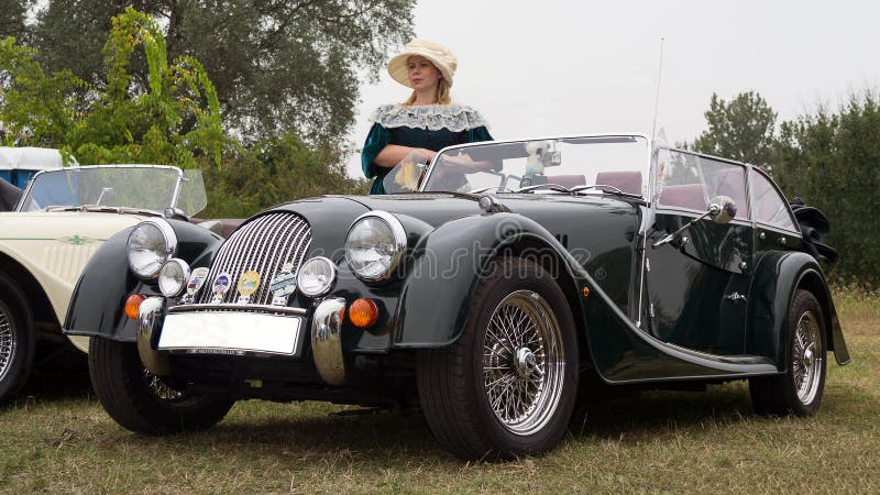 Kvinna i tappningklänning och den klassiska Morgan sportbilen arkivbild Kvinna i tappningklänning och den klassiska Morgan sportbilen arkivbild
