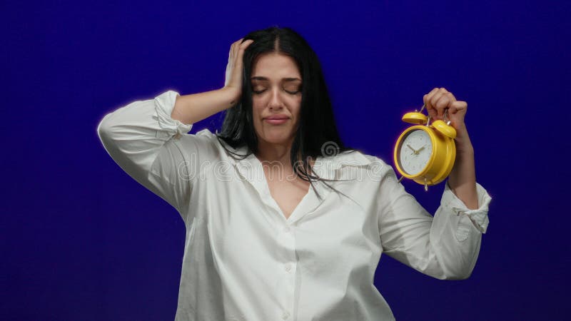 Kvinna med gul larmklocka med trötthetsuttryck över isolerad blå bakgrund i en studio arkivfoto