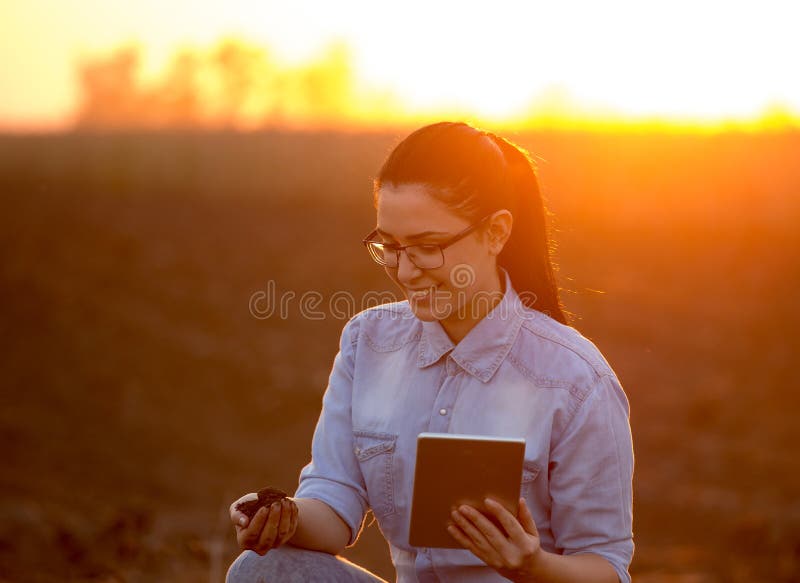 Pretty young engineer woman holding dirt in hand and tablet. Researching soil in field. Pretty young engineer woman holding dirt in hand and tablet. Researching soil in field