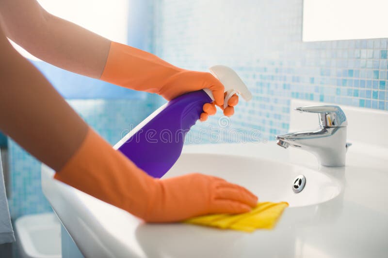 Woman doing chores in bathroom at home, cleaning sink and faucet with spray detergent. Cropped view. Woman doing chores in bathroom at home, cleaning sink and faucet with spray detergent. Cropped view