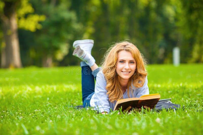 Kvinna som ligger i gräs och läsning en bok