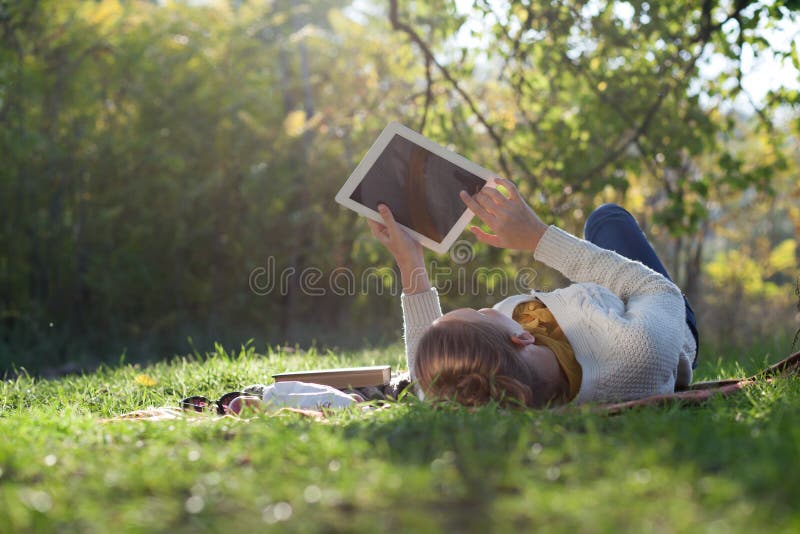 Woman lying on bedding on green grass with ipad during picnic in the park. Woman lying on bedding on green grass with ipad during picnic in the park