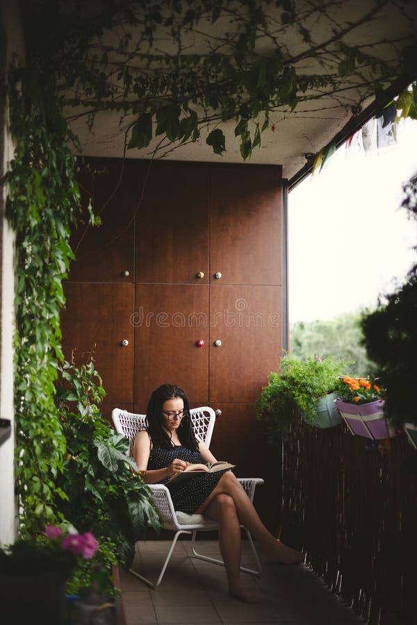 Kvinna som läser en bok på en grön balkong