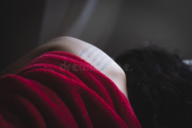 Kvinna som sover med en filt. En vacker kvinna med långt hår som sover i rummet med en röd filt och tatuering i ryggen.