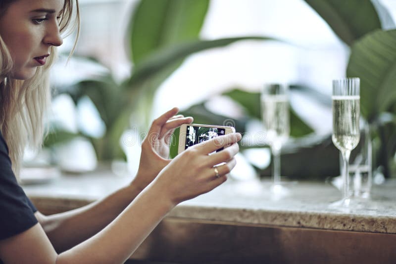 Kvinna som tar fotoet av champagne i exponeringsglas Möte i stadsrestaurang eller kafé Houseplants near fönstret, dagsljus royaltyfri fotografi Kvinna som tar fotoet av champagne i exponeringsglas Möte i stadsrestaurang eller kafé Houseplants near fönstret, dagsljus royaltyfri fotografi