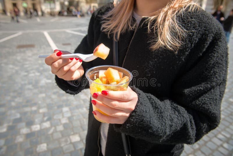 Kvinna som äter fruktsallad från lunchasken i staden arkivbild Kvinna som äter fruktsallad från lunchasken i staden arkivbild