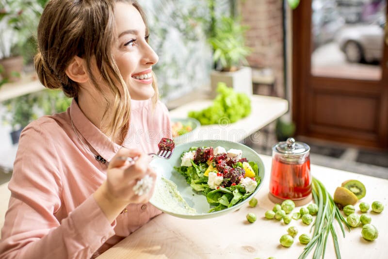 Young woman eating healthy food sitting in the beautiful interior with green flowers on the background. Young woman eating healthy food sitting in the beautiful interior with green flowers on the background