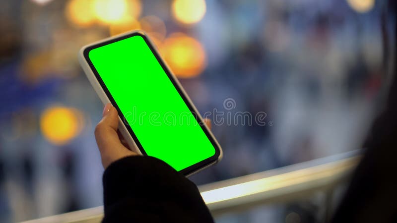 Kvinnainnehavmobiltelefon med den gröna skärmen som står i köpcentrum, annons fotografering för bildbyråer Kvinnainnehavmobiltelefon med den gröna skärmen som står i köpcentrum, annons fotografering för bildbyråer