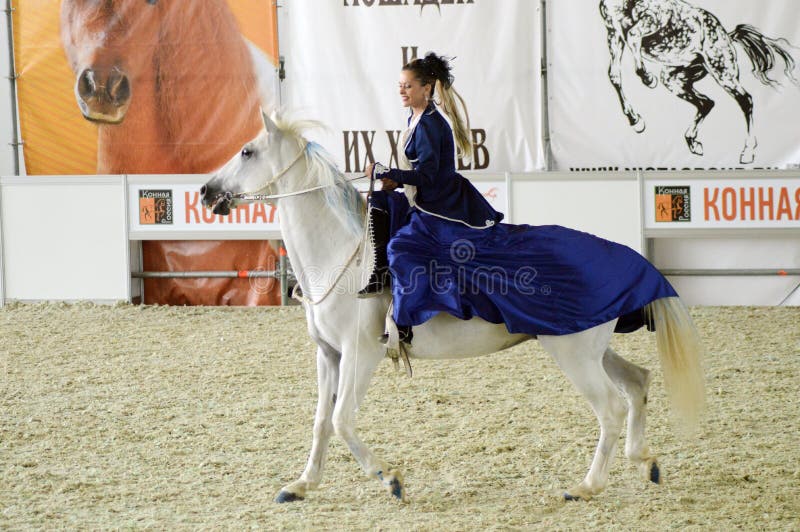 Kvinnajockey i ett mörker - blå klänning som rider en vit häst Under showen Internationell rid- utställningMoskva royaltyfria foton Kvinnajockey i ett mörker - blå klänning som rider en vit häst Under showen Internationell rid- utställningMoskva royaltyfria foton