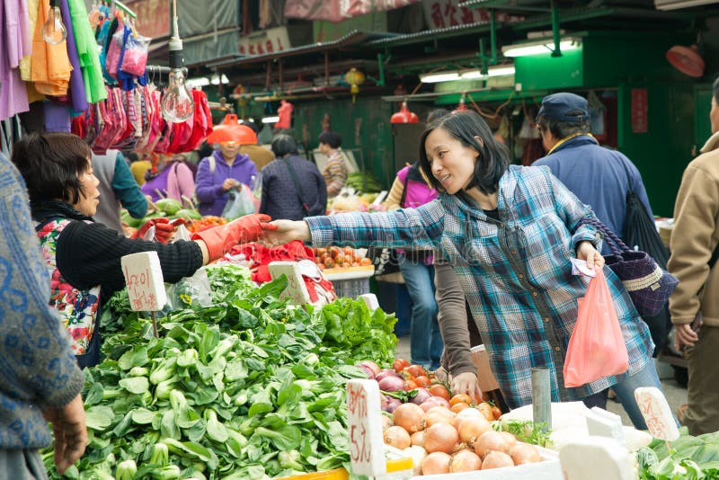 Kvinnaköpandegrönsaker i gatamarknaden, Hong Kong