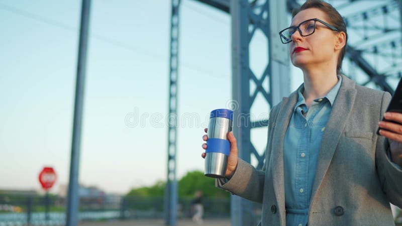 Kvinnan i en rock som går runt i staden tidigt på morgonen och dricker kaffe