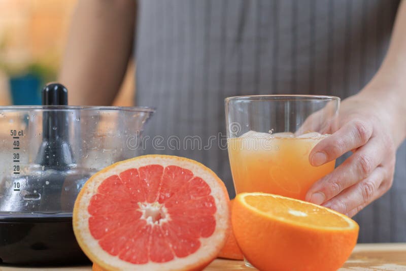 Kvinnan rymmer ny orange fruktsaft i exponeringsglaset med iskuben arkivfoton Kvinnan rymmer ny orange fruktsaft i exponeringsglaset med iskuben arkivfoton