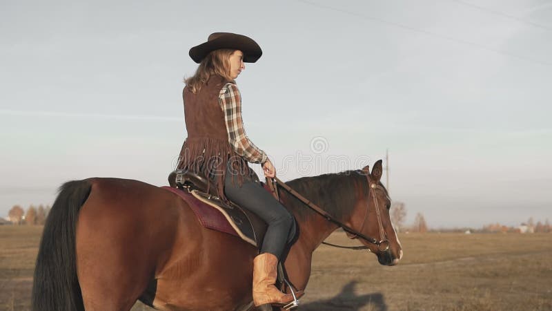 Kvinnaridninghäst i fält Ung cowgirl på den bruna hästen utomhus