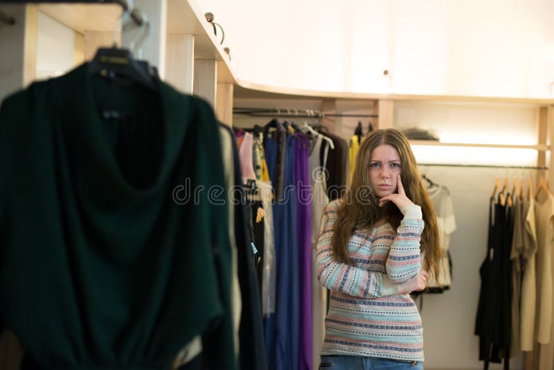 Kvinnashopping som väljer klänningar som ser i den osäkra spegeln fotografering för bildbyråer Kvinnashopping som väljer klänningar som ser i den osäkra spegeln fotografering för bildbyråer