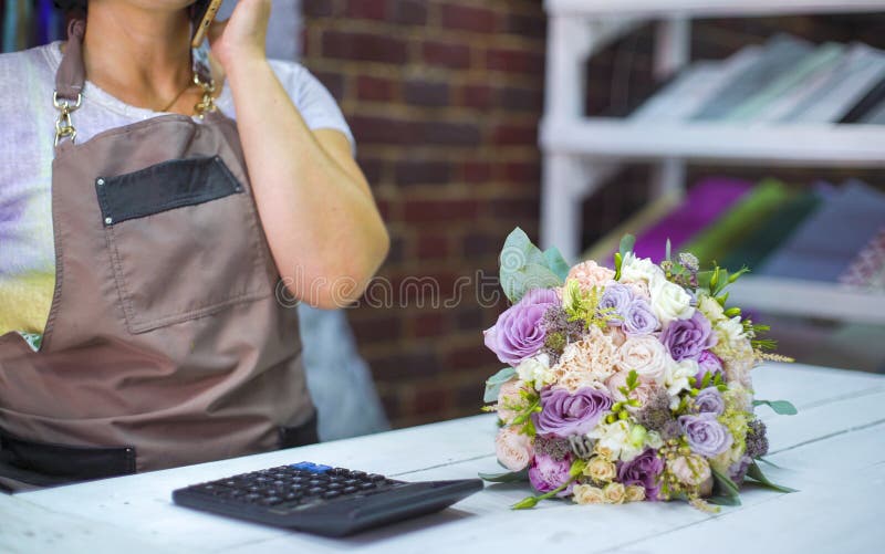 Kvinnlig blomsterhandlare som talar på telefonen som diskuterar kostnad av buketten med kunden i en blomsterhandel royaltyfria foton Kvinnlig blomsterhandlare som talar på telefonen som diskuterar kostnad av buketten med kunden i en blomsterhandel royaltyfria foton