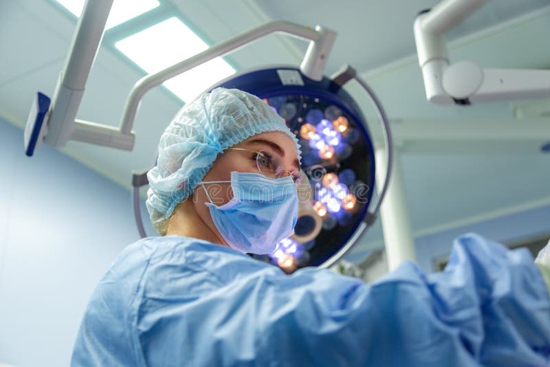 Kvinnlig doktor i kirurgifungerande sjukhusrum Kirurgläkare i skyddande arbetskläderhandskar, maskering och lock royaltyfri bild