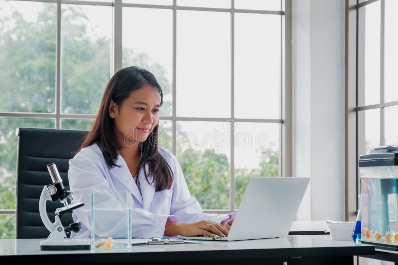 Kvinnlig doktor Sitting At Desk som arbetar på bärbara datorn arkivbild Kvinnlig doktor Sitting At Desk som arbetar på bärbara datorn arkivbild