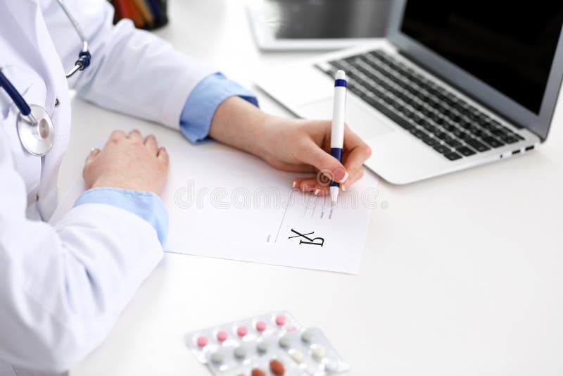 Kvinnlig form f?r doktorsp?fyllningrecept, medan sitta p? skrivbordet i sjukhuscloseup Sjukv?rd f?rs?kring och royaltyfri bild Kvinnlig form f?r doktorsp?fyllningrecept, medan sitta p? skrivbordet i sjukhuscloseup Sjukv?rd f?rs?kring och royaltyfri bild