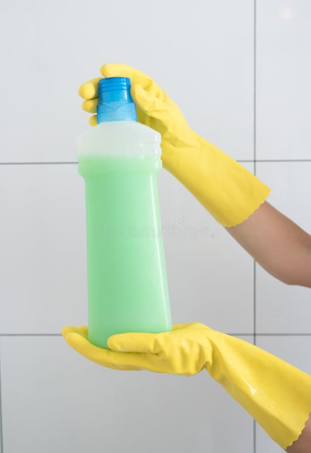 Kvinnlig hand i en rubber handskeinnehavflaska med tvättmedel royaltyfri bild Kvinnlig hand i en rubber handskeinnehavflaska med tvättmedel royaltyfri bild