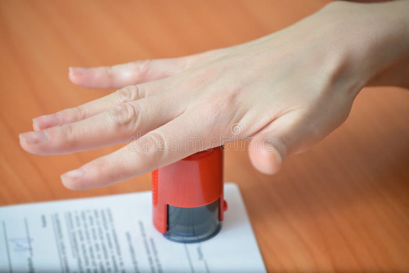Kvinnlig hand som skjuter rubber stämplar på dokument på kontorstabellen, closeupdetaljfors arkivfoto Kvinnlig hand som skjuter rubber stämplar på dokument på kontorstabellen, closeupdetaljfors arkivfoto