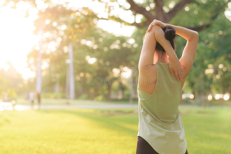 Kvinnlig joggare. lämplig ung asiatisk kvinna med grönt sportkläder som spänner muskeln i parken innan hon går och njuter av en fr royaltyfria bilder