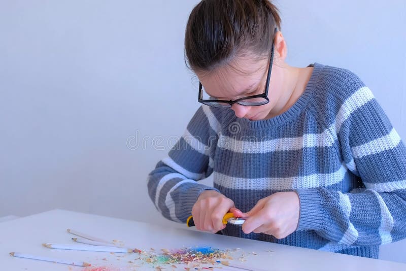 Young woman painter artist in glasses sharpening pencil using sharp knife in art studio. Teacher sharpen pencils for her students on white table. Preparing to work in art studio. Young woman painter artist in glasses sharpening pencil using sharp knife in art studio. Teacher sharpen pencils for her students on white table. Preparing to work in art studio.