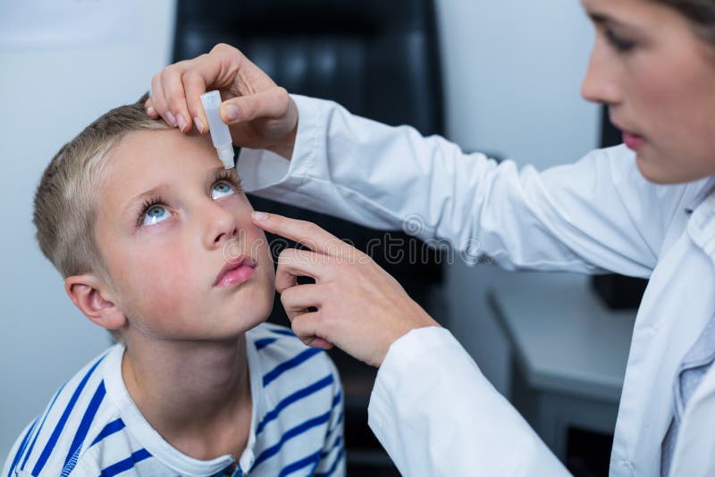 Kvinnlig optometriker som sätter ögondroppe i unga tålmodiga ögon royaltyfria bilder Kvinnlig optometriker som sätter ögondroppe i unga tålmodiga ögon royaltyfria bilder
