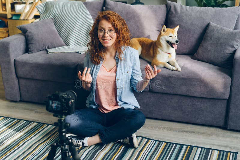 Kvinnlig vlogger som hemma antecknar videoen med den gulliga hunden som sitter på golv genom att använda kameran royaltyfri fotografi Kvinnlig vlogger som hemma antecknar videoen med den gulliga hunden som sitter på golv genom att använda kameran royaltyfri fotografi