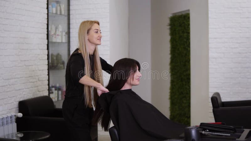 Kvinnliga frisörer har precis avslutat arbetet med sin kvinnliga klient med långt, rakt brunt hår Kvinnor ler och