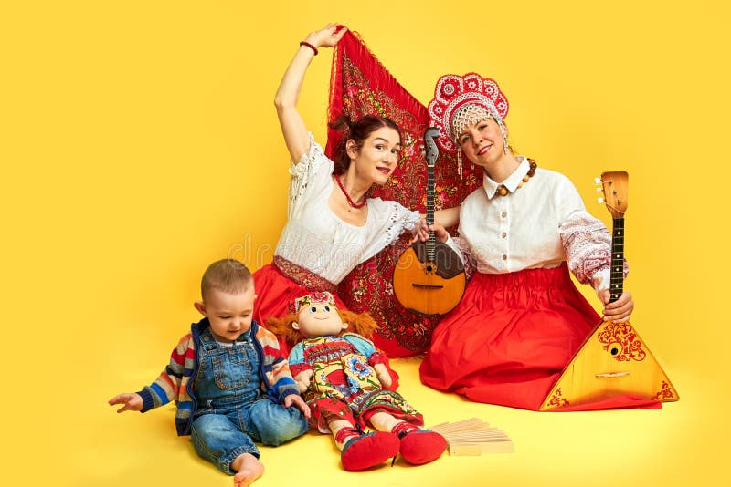 Kvinnliga musiker i ryska folkklänningar med musikinstrument på gul studiobas bakgrund. glada artister från Ryssland royaltyfri bild