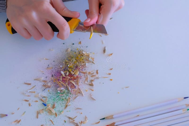 Woman painter artist sharpening yellow pencil using sharp knife, hands closeup. Teacher sharpen blue pencil for her students on white table. Preparing to work in art studio. Woman painter artist sharpening yellow pencil using sharp knife, hands closeup. Teacher sharpen blue pencil for her students on white table. Preparing to work in art studio.