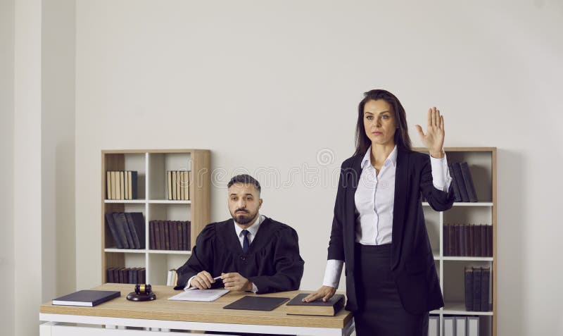 Witness takes an oath before giving a sworn testimony in a court trial. Woman standing near the judge in the courtroom swears on the Holy Bible that she will tell the truth and nothing but the truth. Witness takes an oath before giving a sworn testimony in a court trial. Woman standing near the judge in the courtroom swears on the Holy Bible that she will tell the truth and nothing but the truth