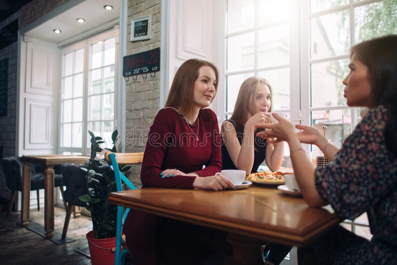 Kvinnliga vänner som dricker kaffe som har en angenäm konversation i en hemtrevlig romantisk restaurang
