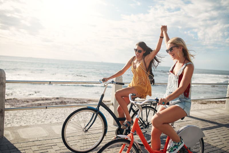 Female friends enjoying cycling on a summer day. Two young female friends riding their bicycles on the seaside promenade. Female friends enjoying cycling on a summer day. Two young female friends riding their bicycles on the seaside promenade.
