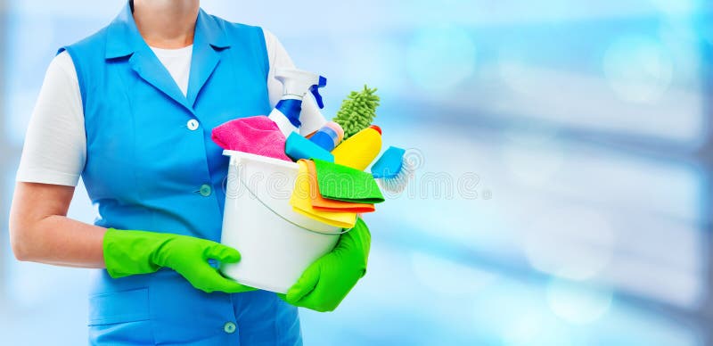 Female housekeeper while cleaning office. Woman wearing protective gloves and holding bucket full of cleaning supplies on blurred background. Female housekeeper while cleaning office. Woman wearing protective gloves and holding bucket full of cleaning supplies on blurred background